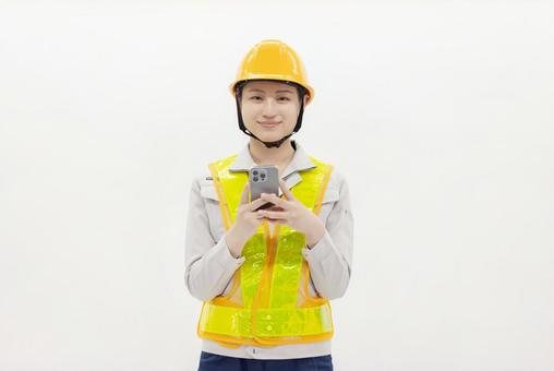 スマートフォンを使う作業服の女性 スマートフォンを使う作業服の女性 女性,作業員,ヘルメットの写真素材