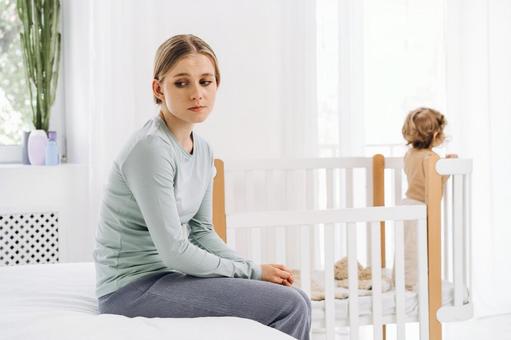 ベッドに座り悩んでいる様子の女性 ベッドに座り悩んでいる様子の女性 育児疲れ,疲れた,座るの写真素材