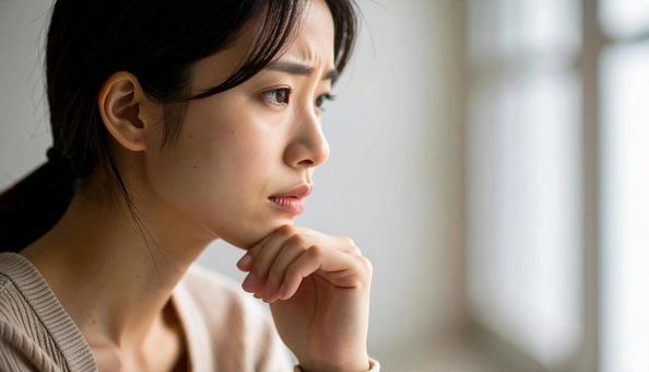 困った顔で手を顎に当てる若い女性の写真