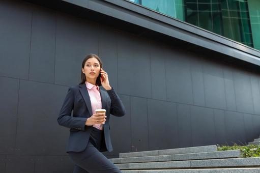 オフィスビルの外の階段でコーヒーを手に電話するビジネスウーマン ビジネスウーマン,ビジネス,女性の写真素材