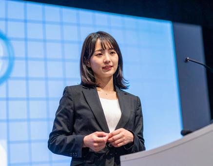 スクリーンの前でプレゼンする女性 スクリーンの前でプレゼンする女性の写真