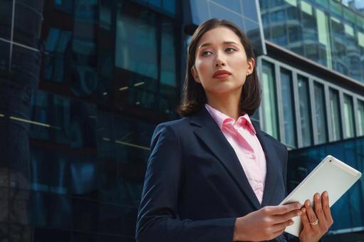 オフィスビルの外でアジア人女性がタブレットを持って立っている ビジネスウーマン,ビジネス,女性の写真素材