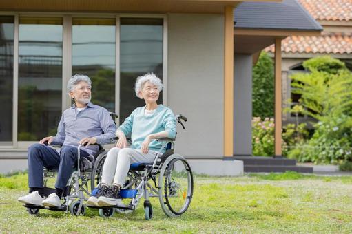 住宅の前で車椅子に乗るシニア夫婦 住宅の前で車椅子に乗るシニア夫婦の写真
