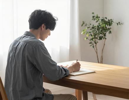 手帳に予定を書き込む若い男性 手帳に予定を書き込む若い男性の写真