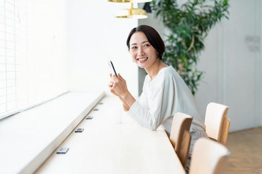 カウンターに座り携帯を持つ女性 スマートフォン,スマホ,女性の写真素材