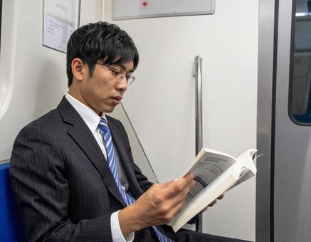電車の中で本を読むビジネスマン男性 電車の中で本を読むビジネスマン男性の写真