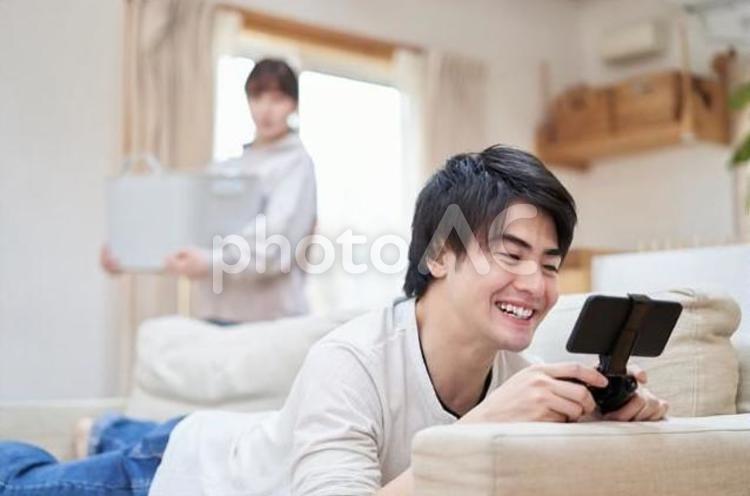家事をする女性とゲームをするアジア人男性 家事,女性,ゲームの写真素材