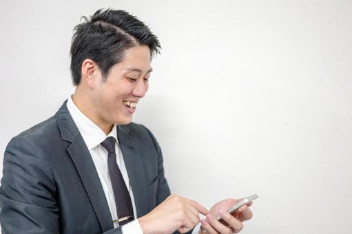笑顔でスマホを触る男性 笑顔でスマホを触る男性 ビジネスマン,スーツ,ネクタイの写真素材