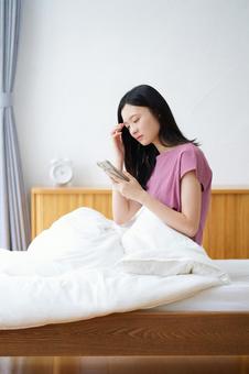 ベッドでスマホを持ち困っている女性 女性,スマートフォン,持つの写真素材