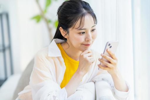 部屋でスマホを操作する女性 スマホ,笑顔,部屋の写真素材