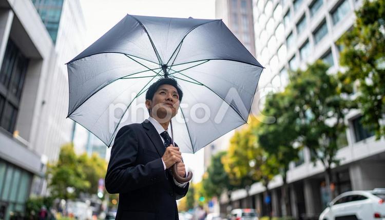 梅雨時、傘をさして街中を歩くビジネスマン 梅雨,雨,傘の写真素材
