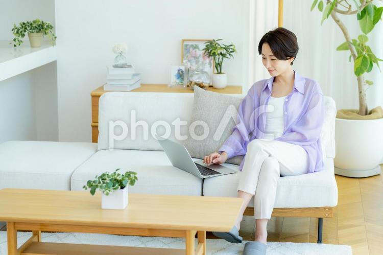 部屋でノートパソコンを使うミドル女性 女性,笑顔,テーブルの写真素材