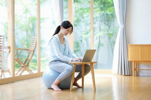 窓際でボールに座りパソコン中の笑顔の女性 女性,バランスボール,ノートパソコンの写真素材