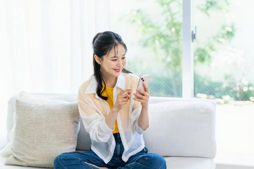 部屋でスマホを操作する女性 部屋でスマホを操作する女性 スマホ,笑顔,部屋の写真素材