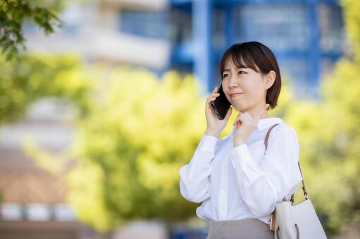 屋外で電話応対をしながら悩む女性社員 スマートフォン,スマホ,携帯電話の写真素材