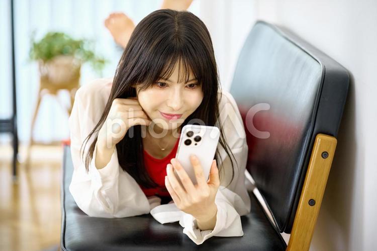 ソファに寝転ぶ女性　スマホを見る スマホ,女性,ソファの写真素材