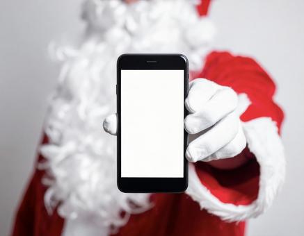 白いスマホの画面を見せるサンタクロースの写真