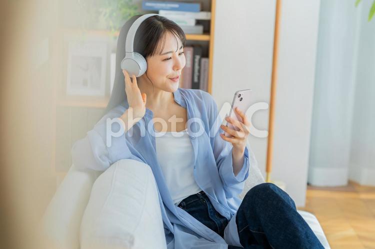 ソファでくつろぐ若い女性 スマホ,ヘッドフォン,ポートレートの写真素材