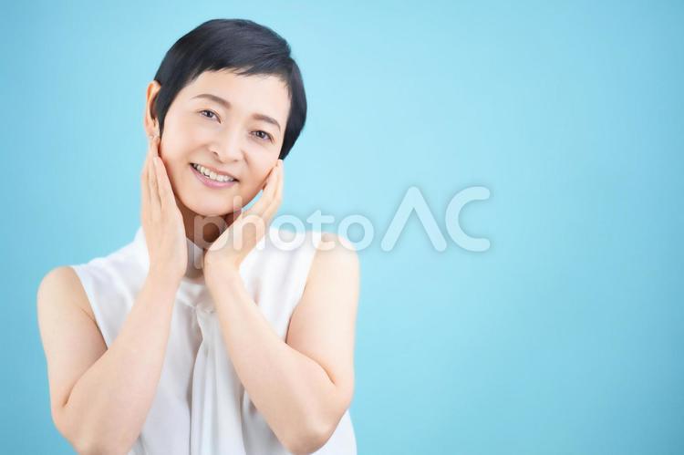 頬を触っているショートカットの女性（水色背景） 女性,日本人,50代の写真素材