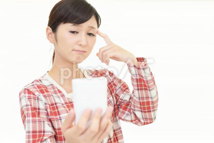 スマートフォンを持つ不安そうな表情の女性 女性,女,スマートフォンの写真素材
