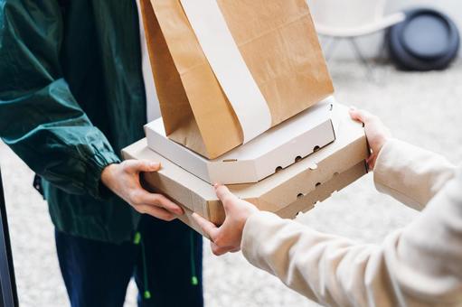 玄関で紙袋とピザ箱を渡す配達員の男性 配達,フードデリバリー,デリバリーの写真素材