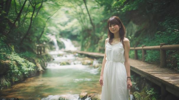 夏の渓流沿いの遊歩道に立つ若い日本人女性 夏の渓流沿いの遊歩道に立つ若い日本人女性の写真