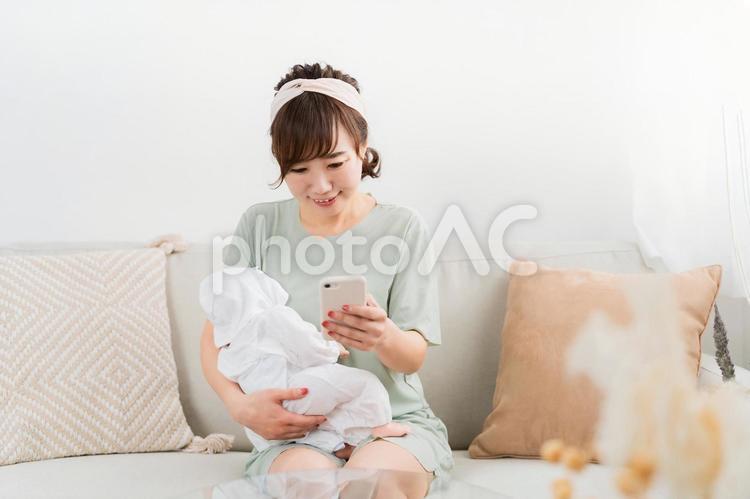 赤ちゃんを抱っこしながらスマホを使う女性 赤ちゃん,スマホ,アプリの写真素材