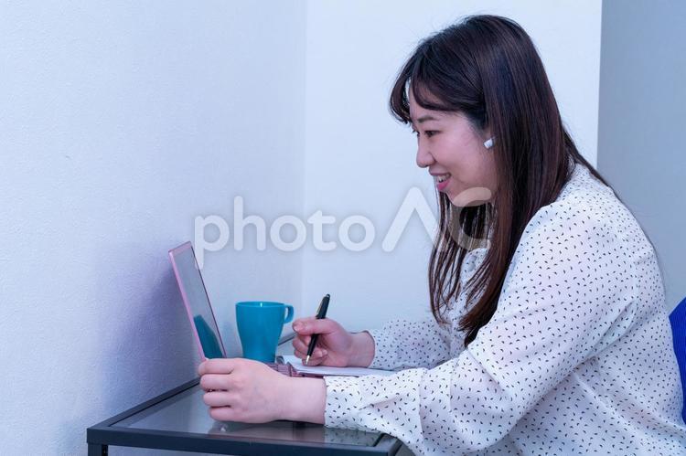画面の同僚と話しながら真面目にリモートワークをする女性	 日本人,リモートワーク,在宅ワークの写真素材