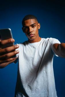 スマートフォンを構えるクールな若者 スマートフォンを構えるクールな若者の写真