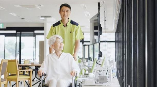 車椅子で散歩をする高齢者と介護士 車椅子で散歩をする高齢者と介護士の写真