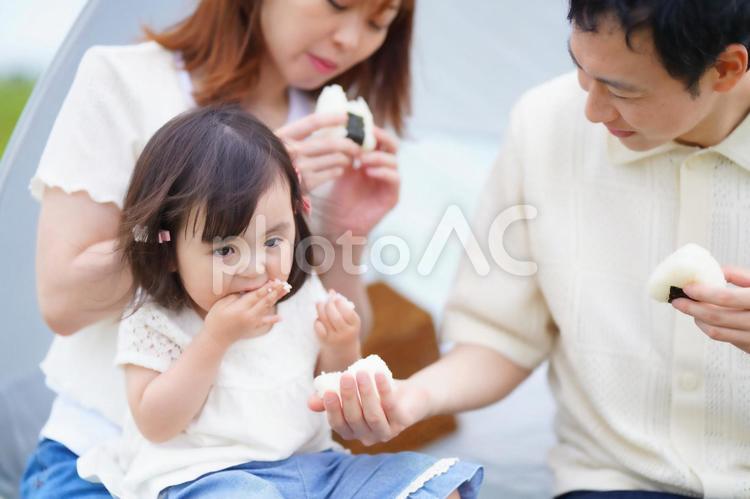 手についた米粒を食べる女の子ととおにぎりを食べる男性と女性 女性,男性,女の子の写真素材