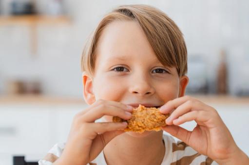 笑顔でフライドチキンを食べている男の子のアップ 笑顔でフライドチキンを食べている男の子のアップの写真