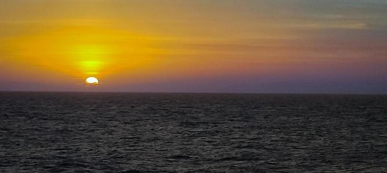 水平線に沈む夕日と黄金色の海の写真