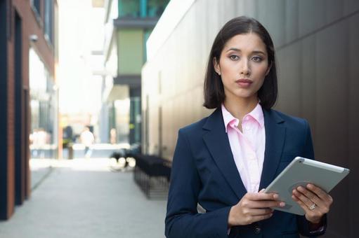 街なかでタブレットを持って立っているスーツのアジア人女性 ビジネスウーマン,ビジネス,女性の写真素材