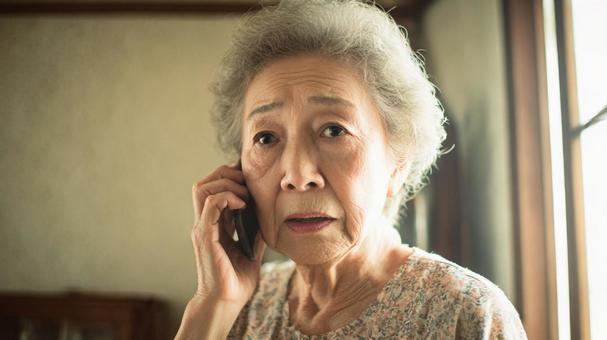 困惑した表情で電話をする高齢女性の写真