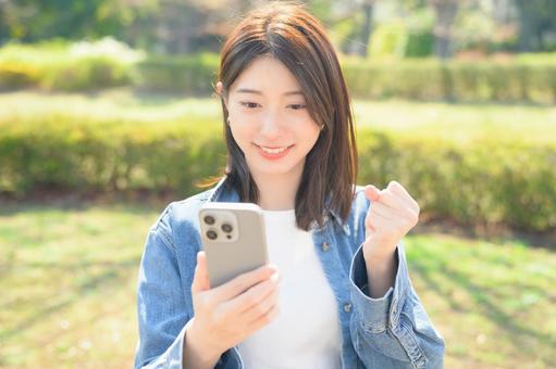 スマホを持ってガッツポーズをする女性 スマホを持ってガッツポーズをする女性の写真