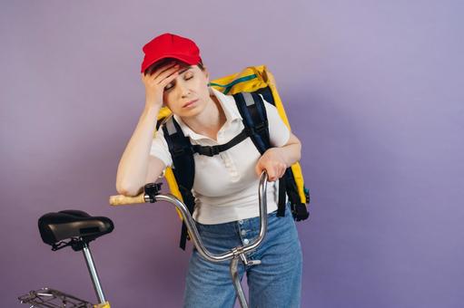自転車にもたれて困っているフードデリバリーの女性 配達,フードデリバリー,デリバリーの写真素材