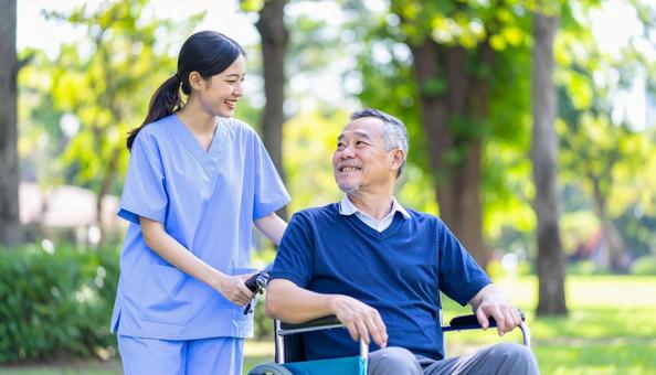 散歩する車椅子の高齢男性と女性介護士 散歩する車椅子の高齢男性と女性介護士の写真