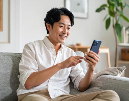 自宅でスマホを操作する男性 自宅でスマホを操作する男性の写真