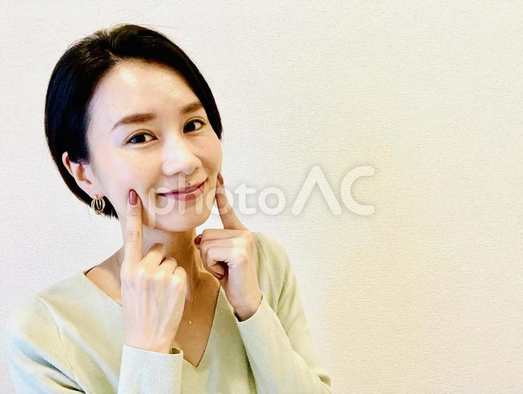 人差し指を顔に当てて微笑む女性 化粧品,化粧水,女性の写真素材