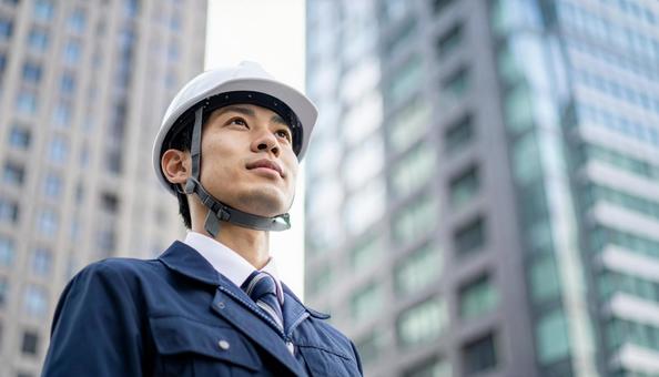 ビル背景に斜め上を見る若い男性建設作業員 ビル背景に斜め上を見る若い男性建設作業員の写真
