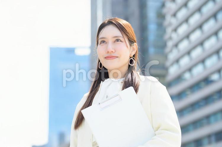 ビル街でバインダーを持って微笑む女性 バインダー,アンケート,キャリアウーマンの写真素材