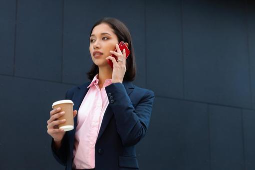オフィスビルの外でコーヒー片手に電話しているビジネスウーマン ビジネスウーマン,ビジネス,女性の写真素材