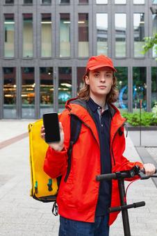 街なかでスマートフォンの画面を見せている配達員の男性 配達,フードデリバリー,デリバリーの写真素材