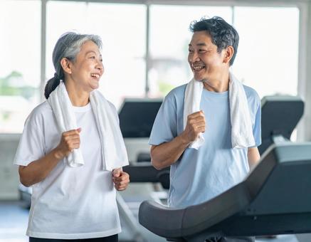 ジムで笑顔で運動する仲良しシニア夫婦 ジムで笑顔で運動する仲良しシニア夫婦の写真