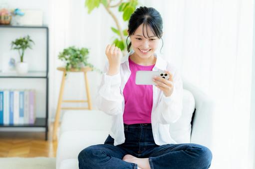 部屋でスマホを操作する若い女性 スマホ,笑顔,若い女性の写真素材