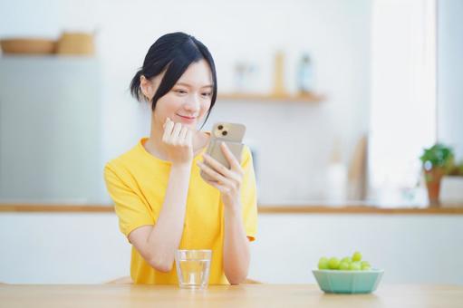 スマホを見て微笑む嬉しそうな黄色の服の女性 女性,スマートフォン,持つの写真素材