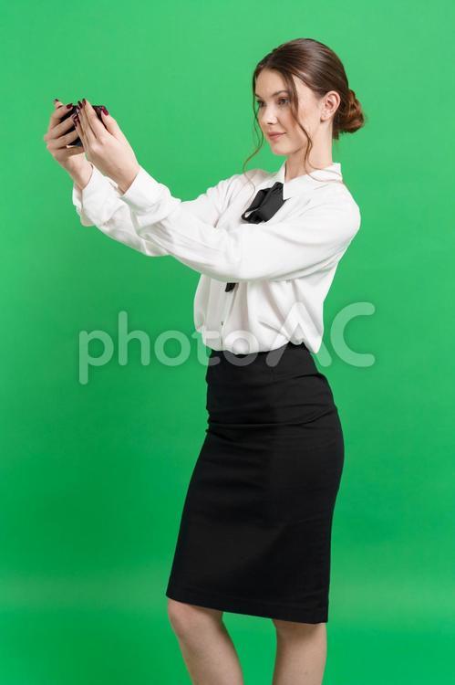 両手で持つスマホを見る横向き女性（緑背景） 女性,スマートフォン,持つの写真素材