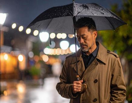 雨の夜にうつむく男性の写真