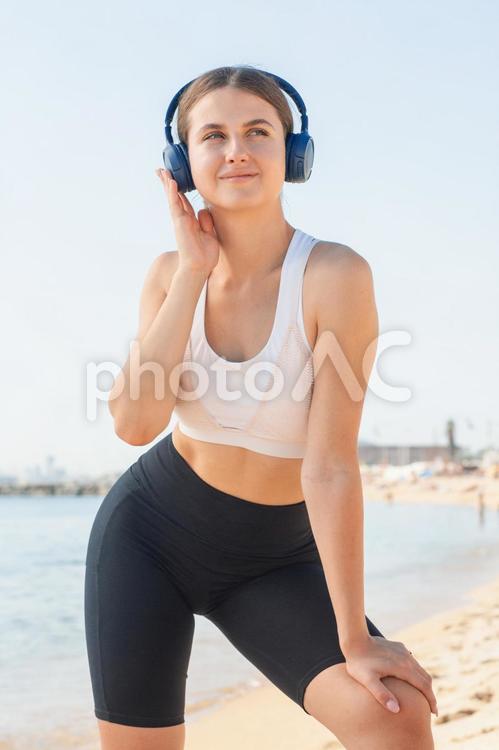 ビーチでヘッドホンをして音楽を聞きながらトレーニングする女性 女性,外国人,欧米人の写真素材